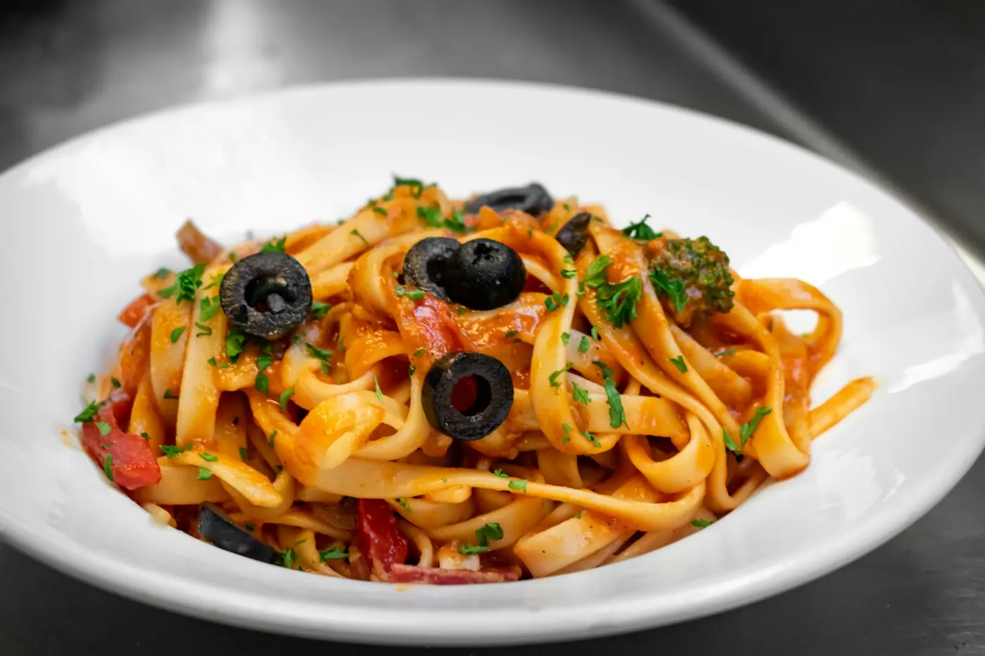 Piatto di fettuccine al pomodoro con olive e basilico, servito in una trattoria